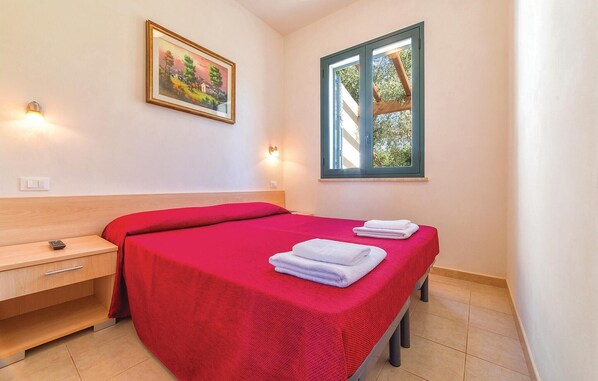 Une chambre d’hôtel avec un lit, une table de chevet, un tableau au mur et une fenêtre donnant sur des arbres.