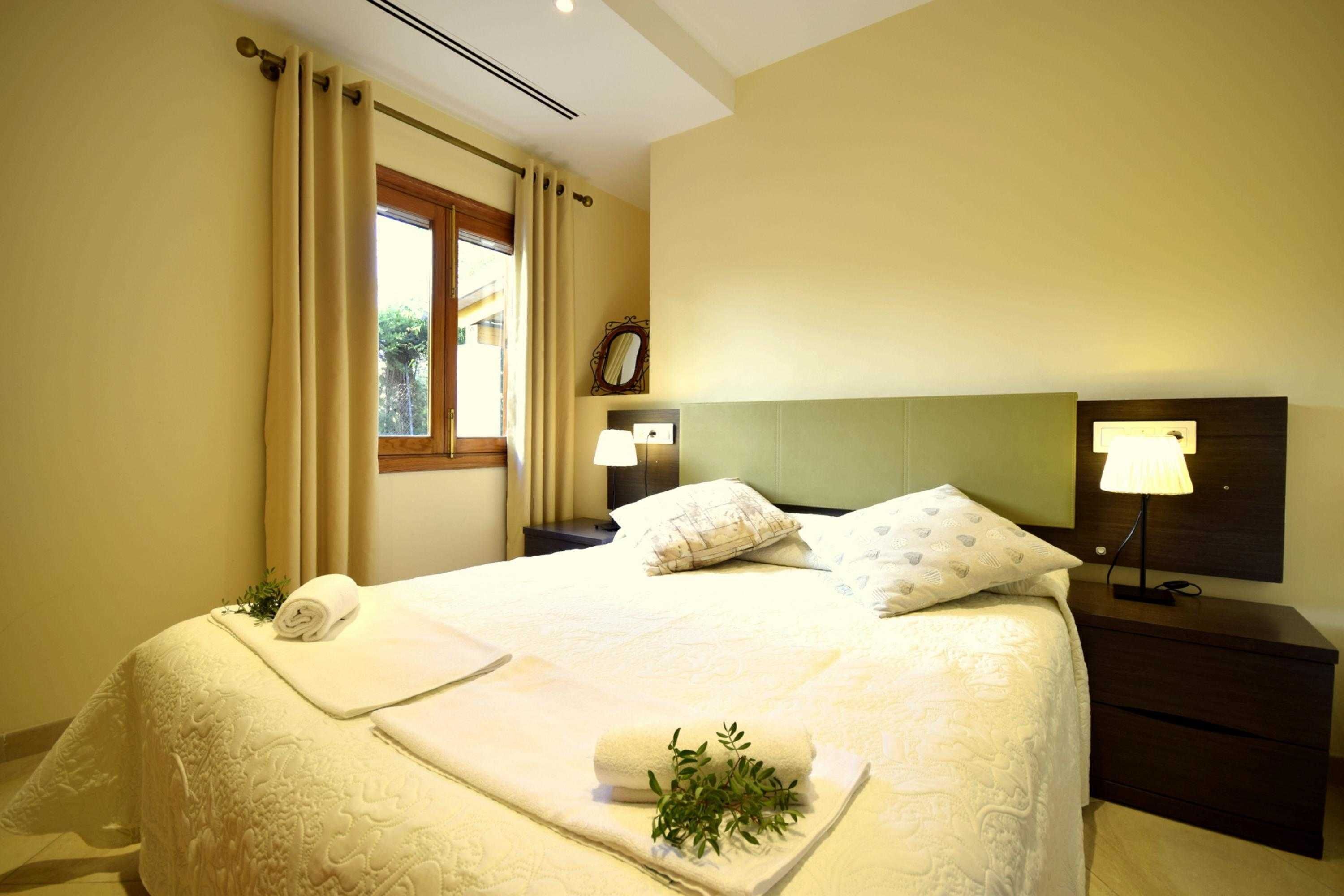 A neatly made bed with a rolled towel and a plant, a bedside lamp, and a nightstand with a lamp.