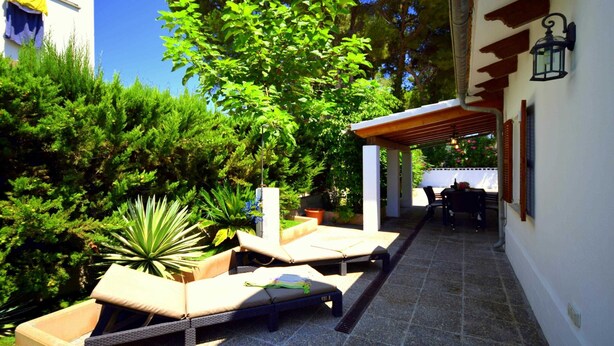 A patio with lounge chairs and a table, surrounded by greenery and a building with a pergola. - 44236 Modern beach house Es Baladre (Alcúdia)