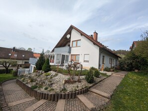 Una casa moderna con un invernadero, un jardín con un sendero de piedra y un patio de ladrillo.