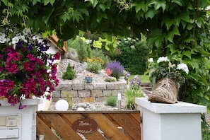 Un jardín con diversas flores y plantas, un muro de piedra y una cerca de madera con un letrero.