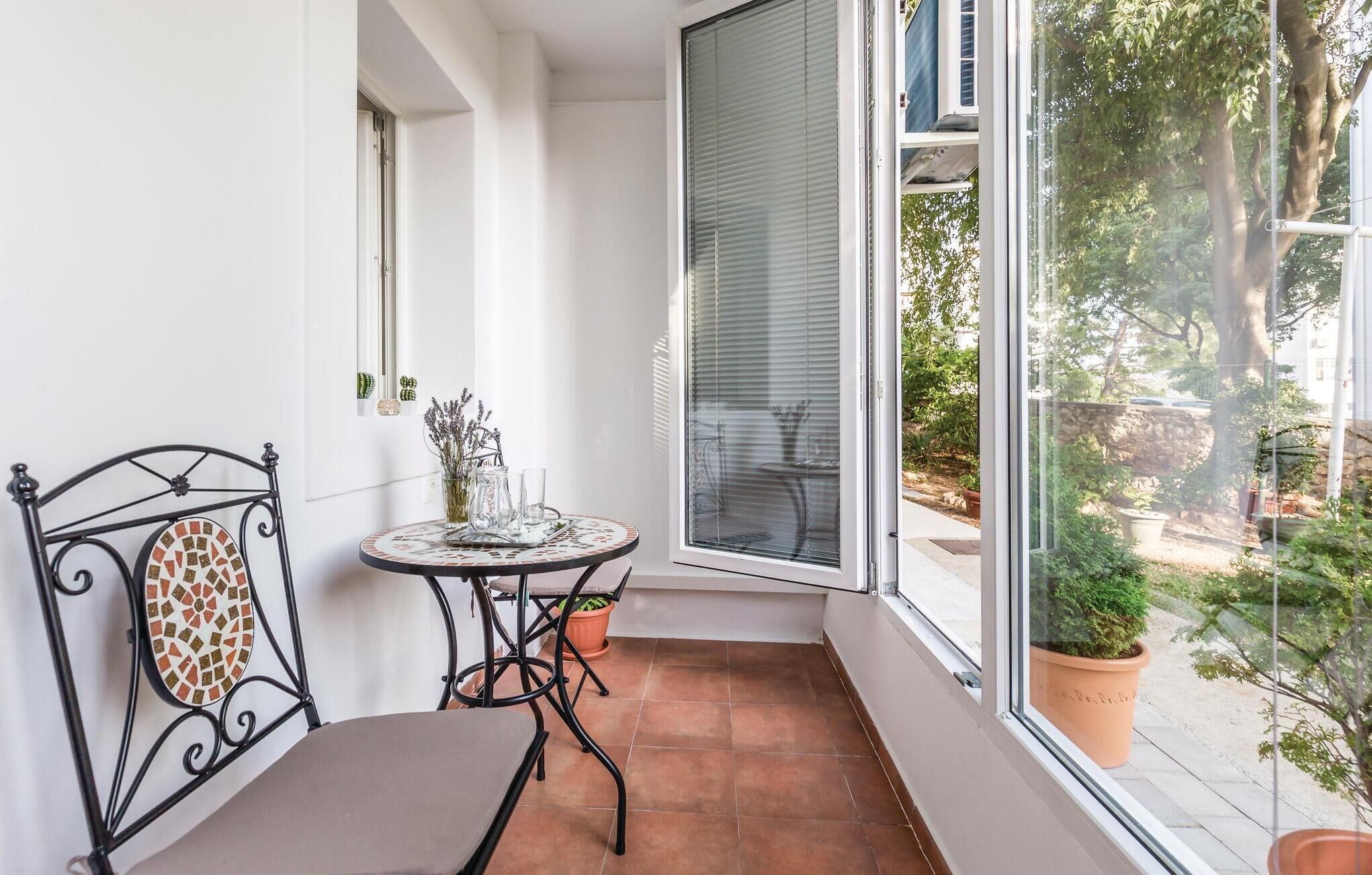 Ein kleiner Balkon mit einem Metallstuhl, einem Tischchen mit Tablett und einem Blumentopf.
