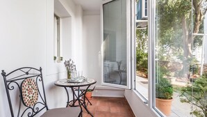 En lille balkon med en metalstol, et lille bord med bakke og en potteplante.