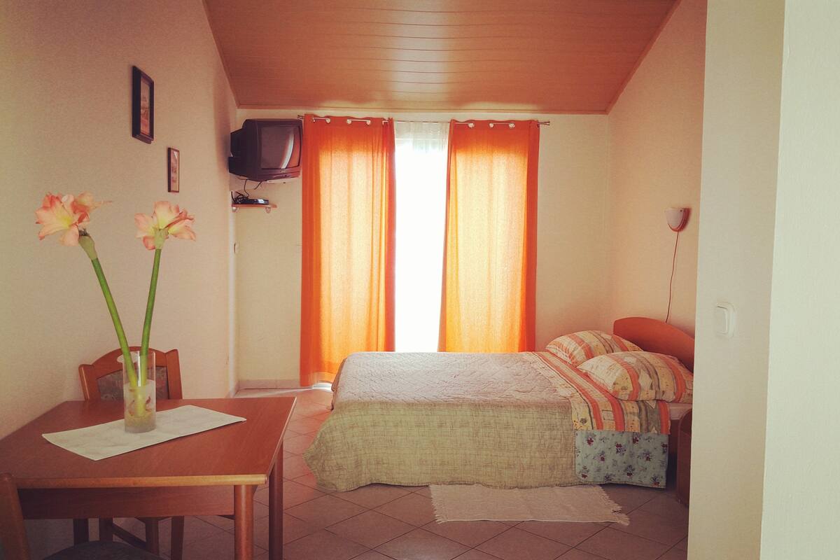 Ein kleiner, gemütlicher Raum mit einem Bett, einem Schreibtisch mit Stuhl und einem an der Wand befestigten Fernseher.