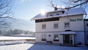 En tvåvåningsbyggnad som heter ”Haus Fink”, med ett snötäckt tak och en klar himmel.
