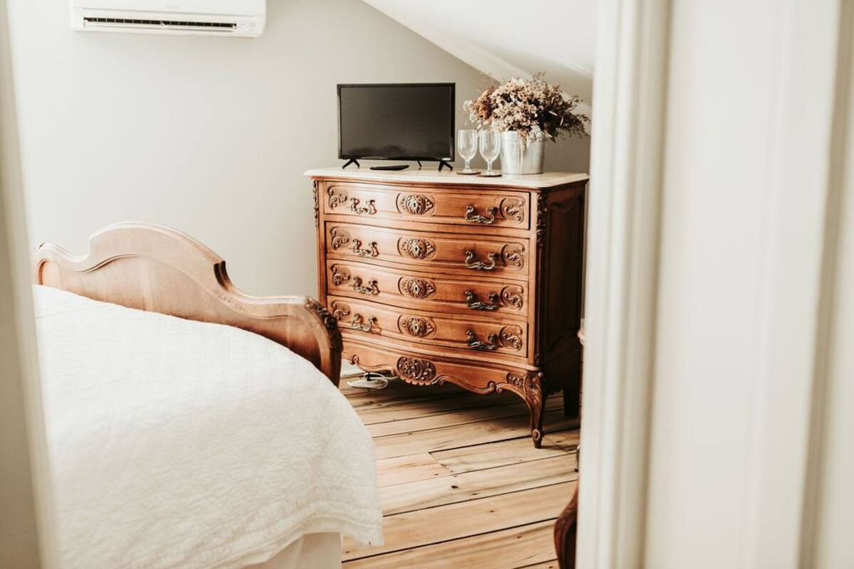 A bedroom with a wooden dresser, a television on top, and a bed with a white bedspread.