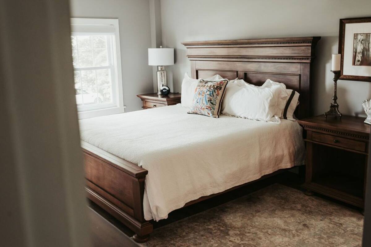 A bedroom with a large bed, wooden headboard, bedside tables with lamps, and a window.