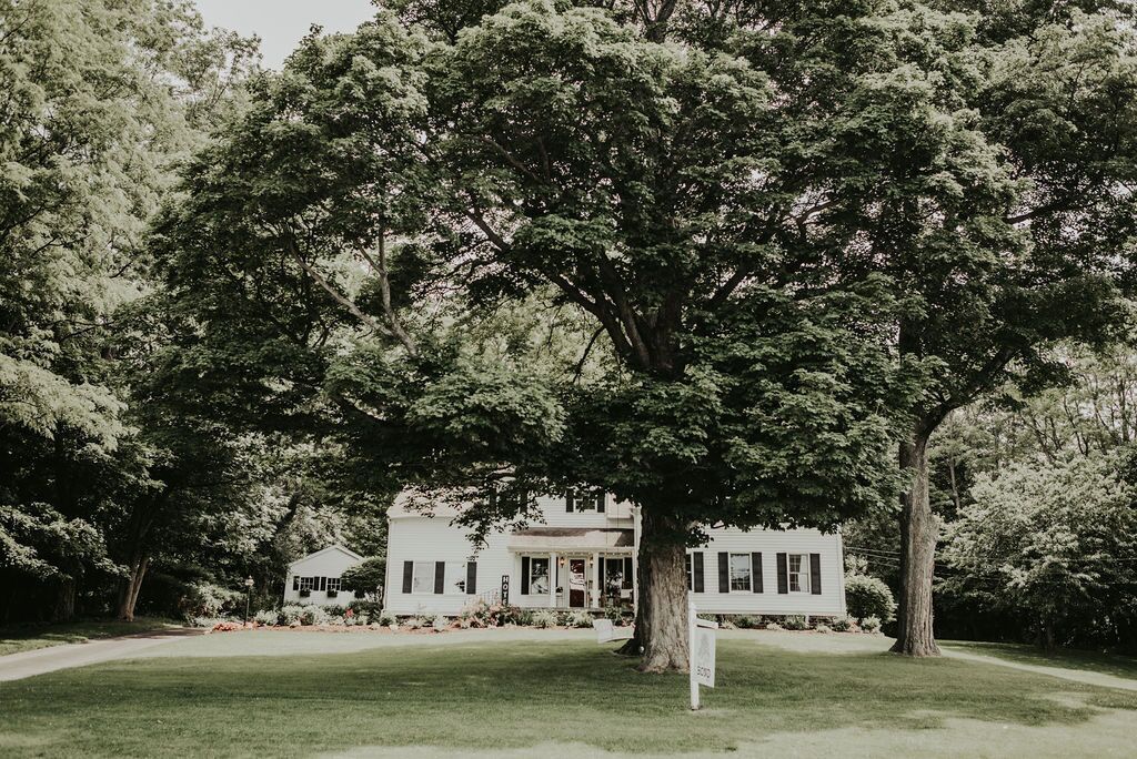 A large white building with a porch, surrounded by lush greenery and a well-maintained lawn.