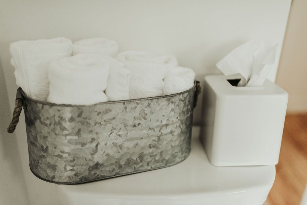 A metal container holding rolled towels and a white tissue box on a toilet.