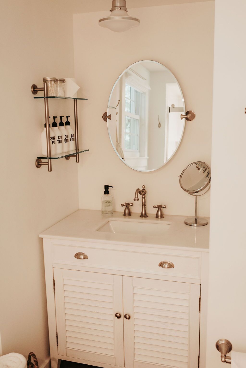 A bathroom with a white vanity, a round mirror, and a shelf with toiletries.