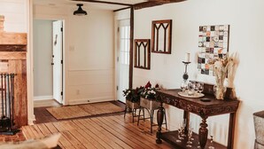 A wooden-floored room with a rustic ceiling, a table set with glasses and flowers, and a wall with a collage of postcards.