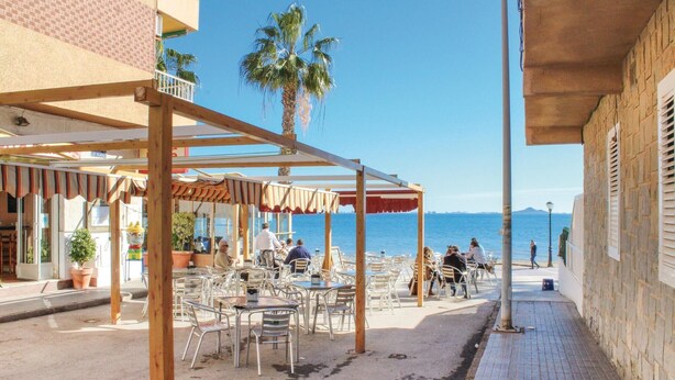 An outdoor café with tables and chairs, a wooden pergola, and a view of the sea. - Stunning apartment in Los Alcazares with WiFi (Los Alcazares)
