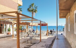 Un café al aire libre con mesas y sillas, una pérgola de madera y vistas al mar.