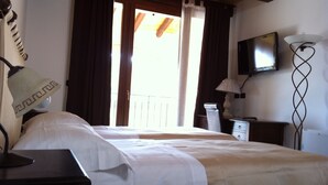 A hotel room with a bed, a desk, a lamp, a television, and a balcony with curtains.