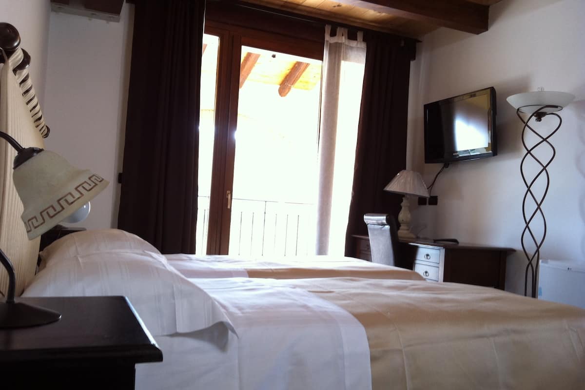 Une chambre d’hôtel équipée d’un lit, d’un bureau, d’une lampe, d’une télévision et d’un balcon avec des rideaux.
