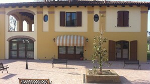 A yellow building with arched doorways, a striped awning, and a small tree in a planter.
