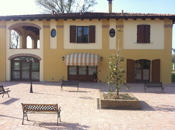 A yellow building with arched doorways, a striped awning, and a small tree in a planter.