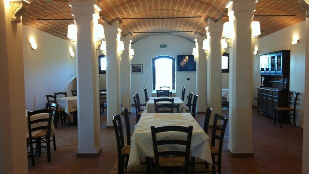 A long dining hall with high ceilings and columns, featuring tables and chairs arranged for dining.
