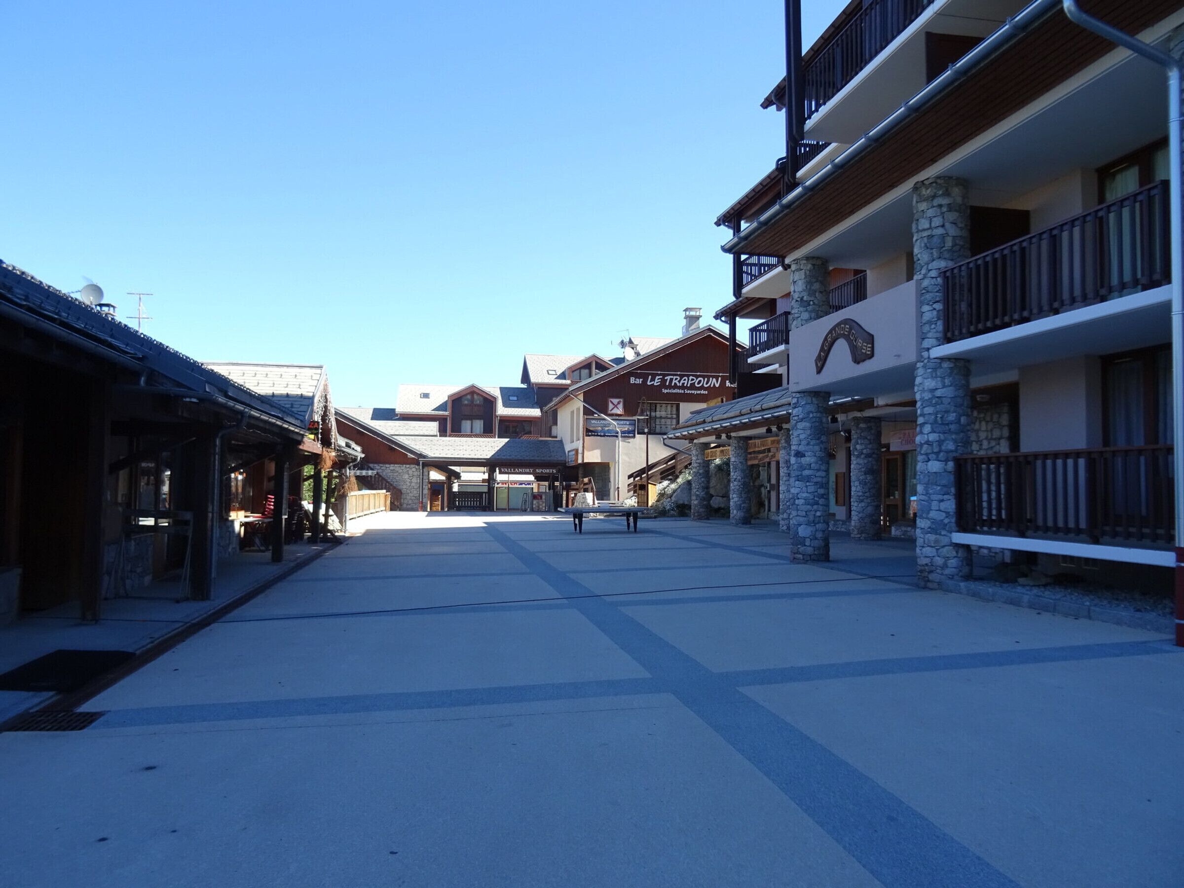 A street with buildings, including a bar named 'Bar Le Trappouin' and a sign for 'Vallandry Sports'.