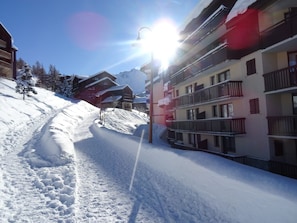 En snötäckt skidbacke med byggnader och en solupplyst himmel.