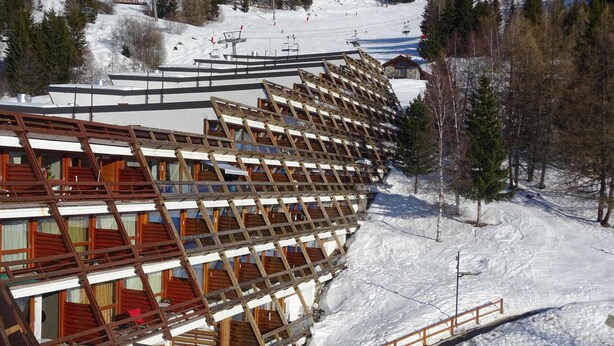 A multi-story building with a sloped roof, wooden balconies, and a ski lift in the background. - Studio Cabin Arc 1600, 5 Persons, Ski-in/Ski-out, WiFi (Les Arcs 1600)