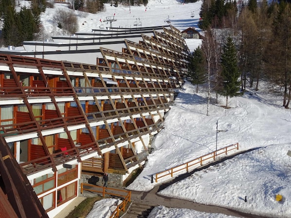 A multi-story building with a sloped roof, wooden balconies, and a ski lift in the background.