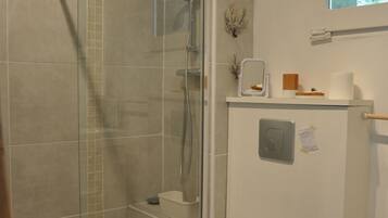 A bathroom with a glass-enclosed shower, a toilet, and a window above the sink.