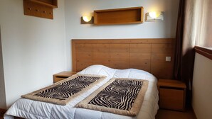 A bedroom with a wooden headboard, a white bedspread, two zebra-patterned throw blankets, two bedside tables, and wall-mounted light fixtures. - 3-room apartment, 8 ppl, Arc 1600, near slopes, pool access & parking (Les Arcs 1600)