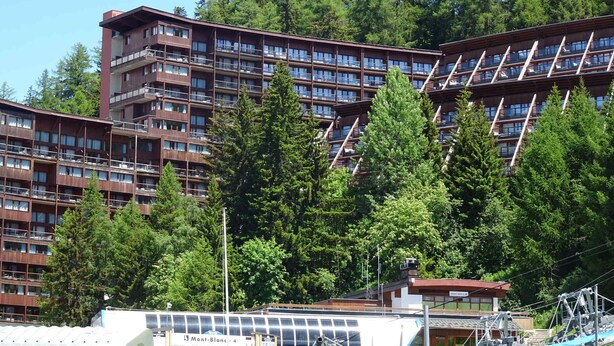 A multi-story hotel with a modern architectural design, featuring balconies and a dense forest backdrop. - 3-room apartment, 8 ppl, Arc 1600, near slopes, pool access & parking (Les Arcs 1600)