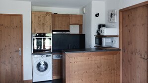 A compact kitchen with wooden cabinets, a washing machine, a microwave, and a coffee maker. - 3-room apartment, 8 ppl, Arc 1600, near slopes, pool access & parking (Les Arcs 1600)