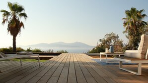 Un terrazzo in legno con mobili da esterno, palme e vista su montagne lontane.