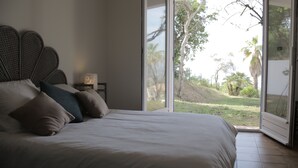 Una camera da letto con un letto grande, un comodino e una finestra vista su spazi verdi e alberi.