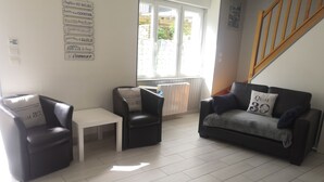 Ein Wohnzimmer mit einer schwarzen Ledersofa, einem weißen Couchtisch und zwei schwarzen Sessel. Ein Fenster bietet Blick ins Freie.