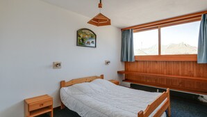 Une chambre à coucher comprenant un lit, une table de chevet, une étagère en bois, une fenêtre avec des rideaux et un tableau accroché au mur.