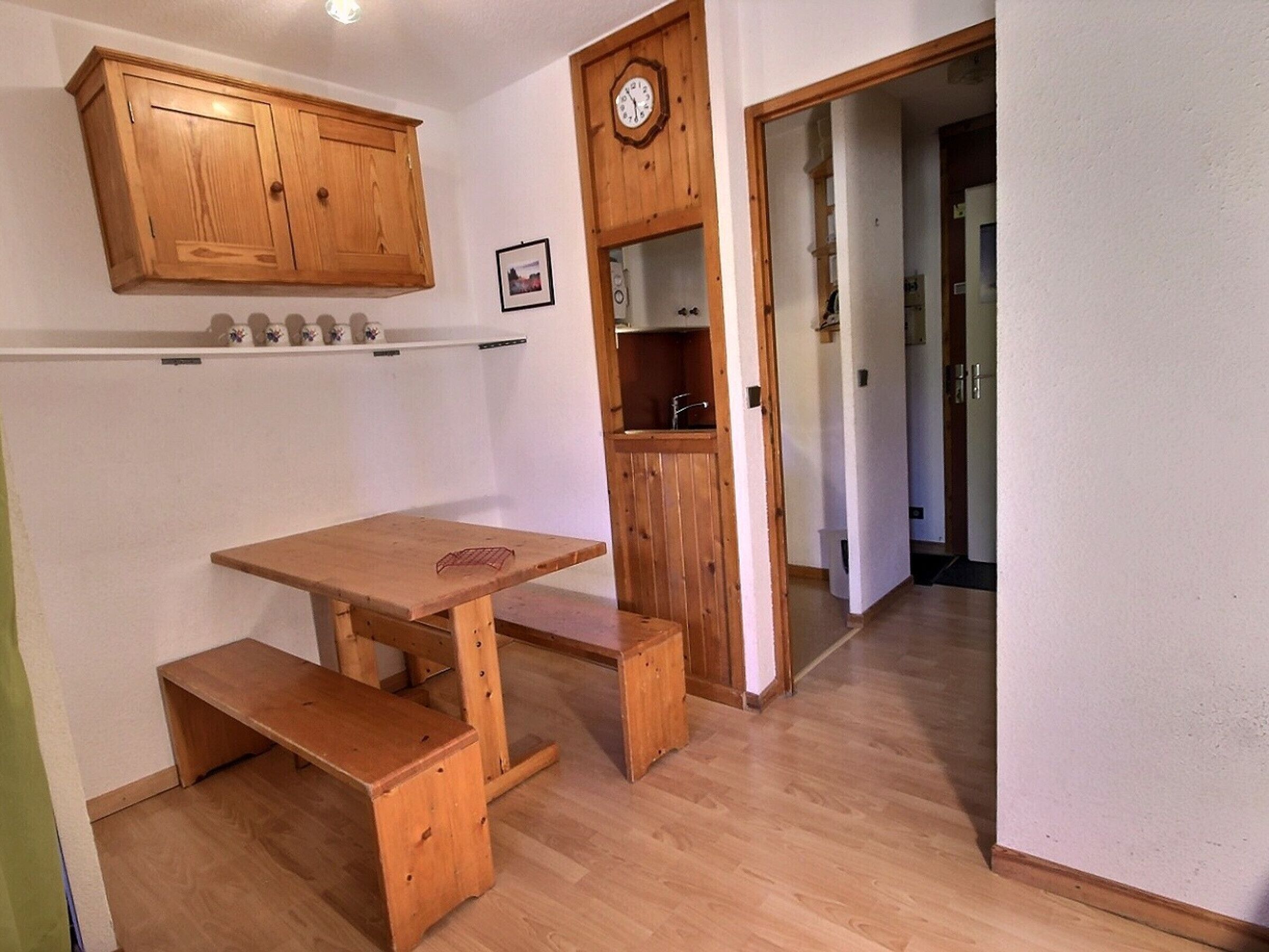 A wooden dining table with benches, a wooden cabinet above, and a clock on the wall.