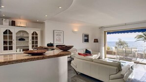 A modern kitchen with a central island, a dining area with a white sofa, and a view of the sea through large windows. - 4 bedrooms - Close to palace - Sea front - Beaches on foot  . Near  Old Port (Cannes)