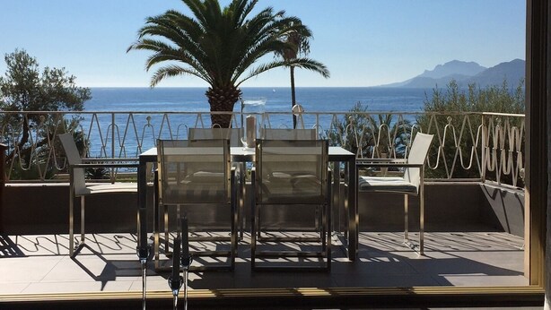 A terrace with a table and chairs, a palm tree, and a view of the sea and mountains. - 4 bedrooms - Close to palace - Sea front - Beaches on foot  . Near  Old Port (Cannes)
