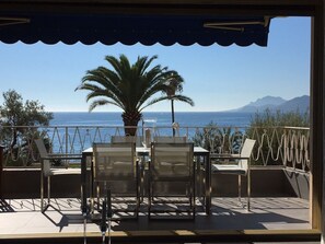 Una terrazza con tavolo e sedie, una palma e vista sul mare e sulle montagne.