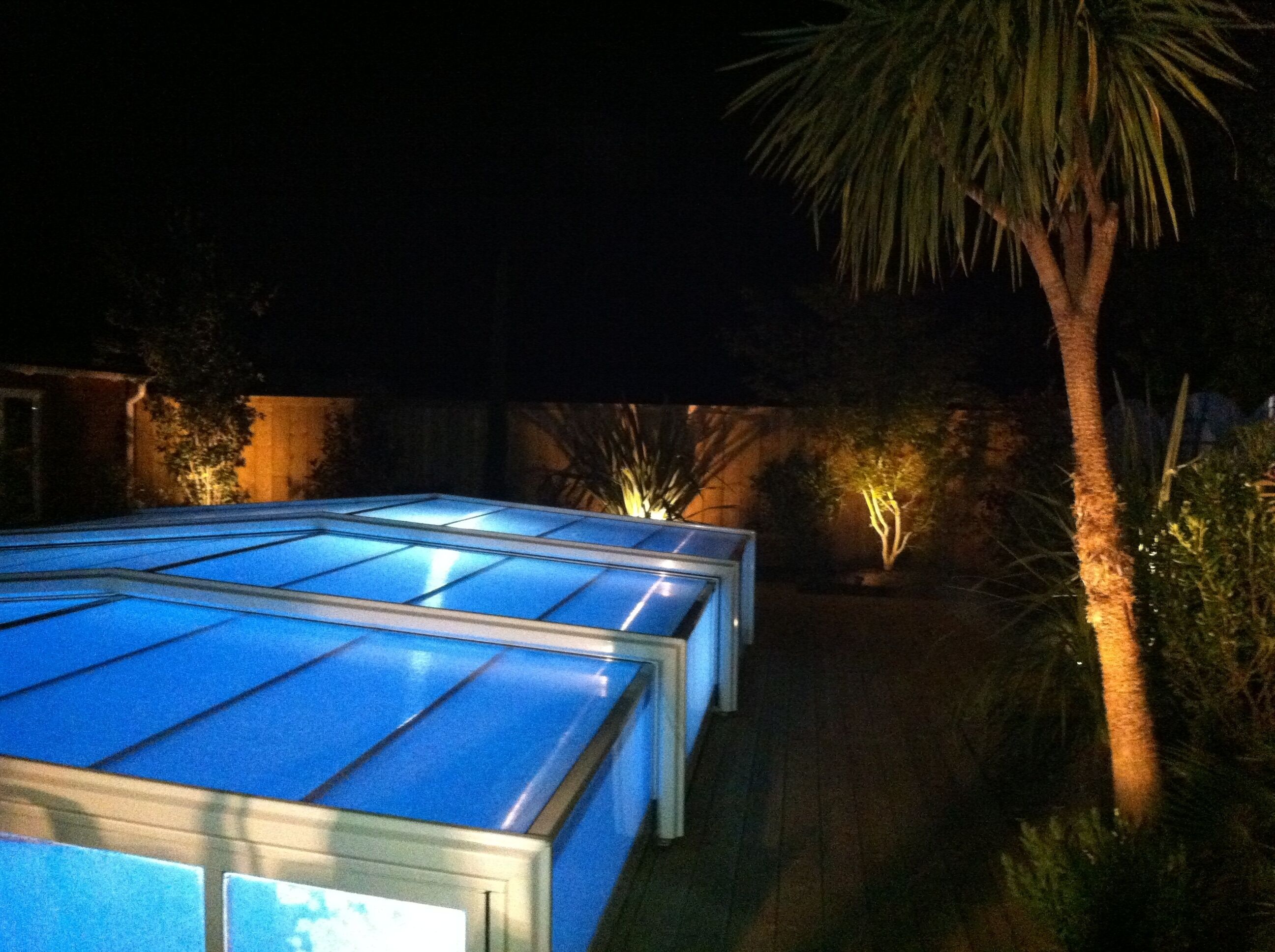 A series of glass-enclosed structures with a reflective surface, surrounded by vegetation and illuminated by artificial lighting.