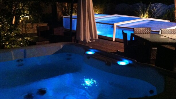 Uma banheira de hidromassagem com iluminação azul, rodeada por móveis de exterior e um terraço.