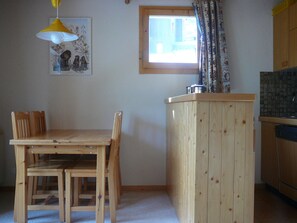Uma cozinha pequena com armários de madeira, uma mesa de jantar com cadeiras, uma janela com cortinas e uma luminária pendente amarela.