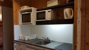 Cocina compacta con microondas, tostadora y hervidor en estantes, un lavamanos y lavavajillas.