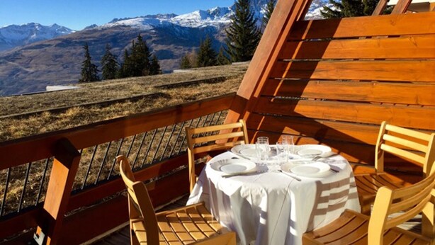 Una terraza de madera con una mesa preparada para dos, con vista a un paisaje montañoso.
