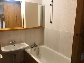 Un baño con un lavamanos blanco, una bañera y un espejo sobre el lavamanos.