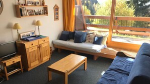 Ett mysigt rum med en säng, en soffa, en tv och ett träbord.