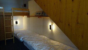 Ett sovsalsrum med våningssängar, en stege och väggmonterade lampor.