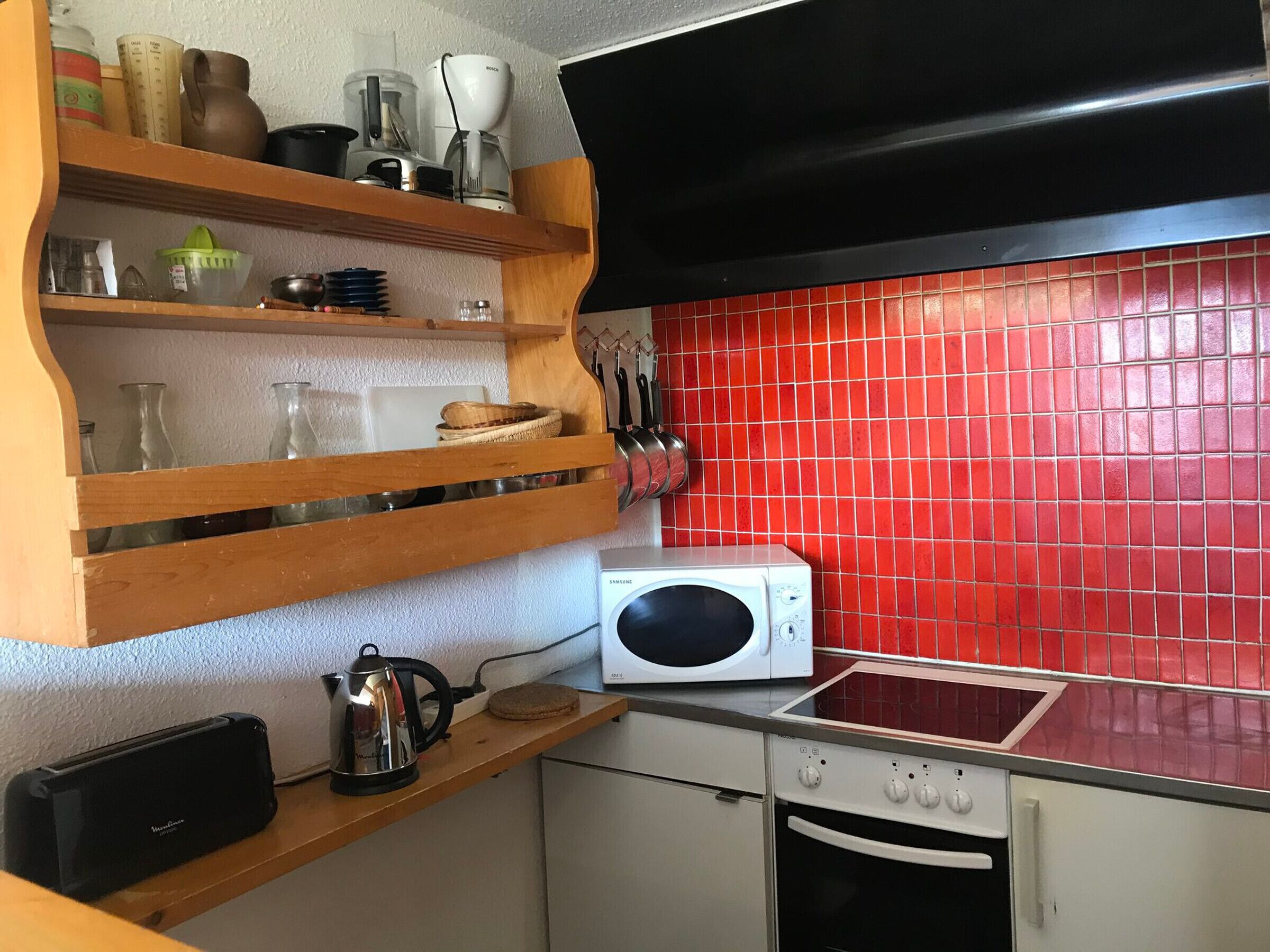 Una cocina con microondas, hervidor y diferentes utensilios en estantes.