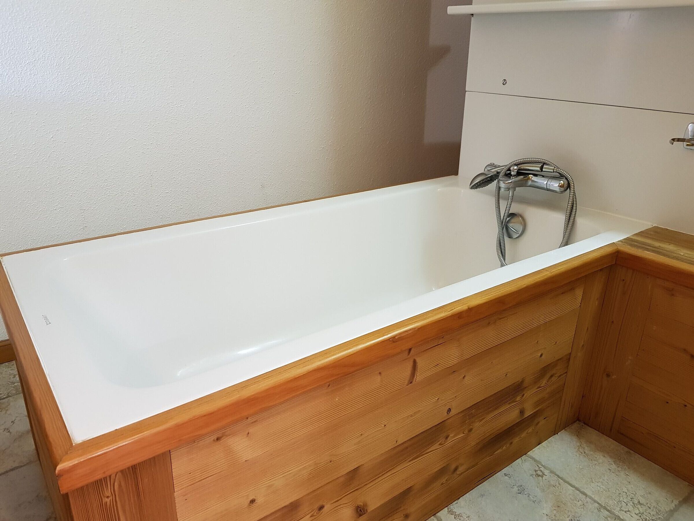 Une salle de bain avec un meuble-lavabo en bois, une baignoire blanche et une pomme de douche.