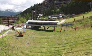 A ski lift station with a cable car on a grassy slope, surrounded by buildings and trees. - Renovated Studio for 3 at Arc 1600, Ski-in, Pets Allowed (Les Arcs 1600)