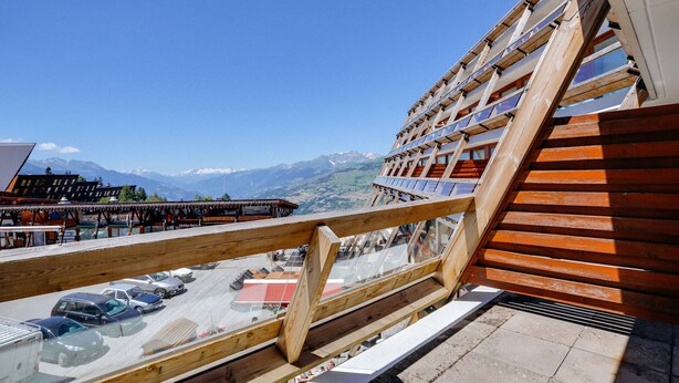 A wooden balcony with a view of a mountain range and a restaurant below.